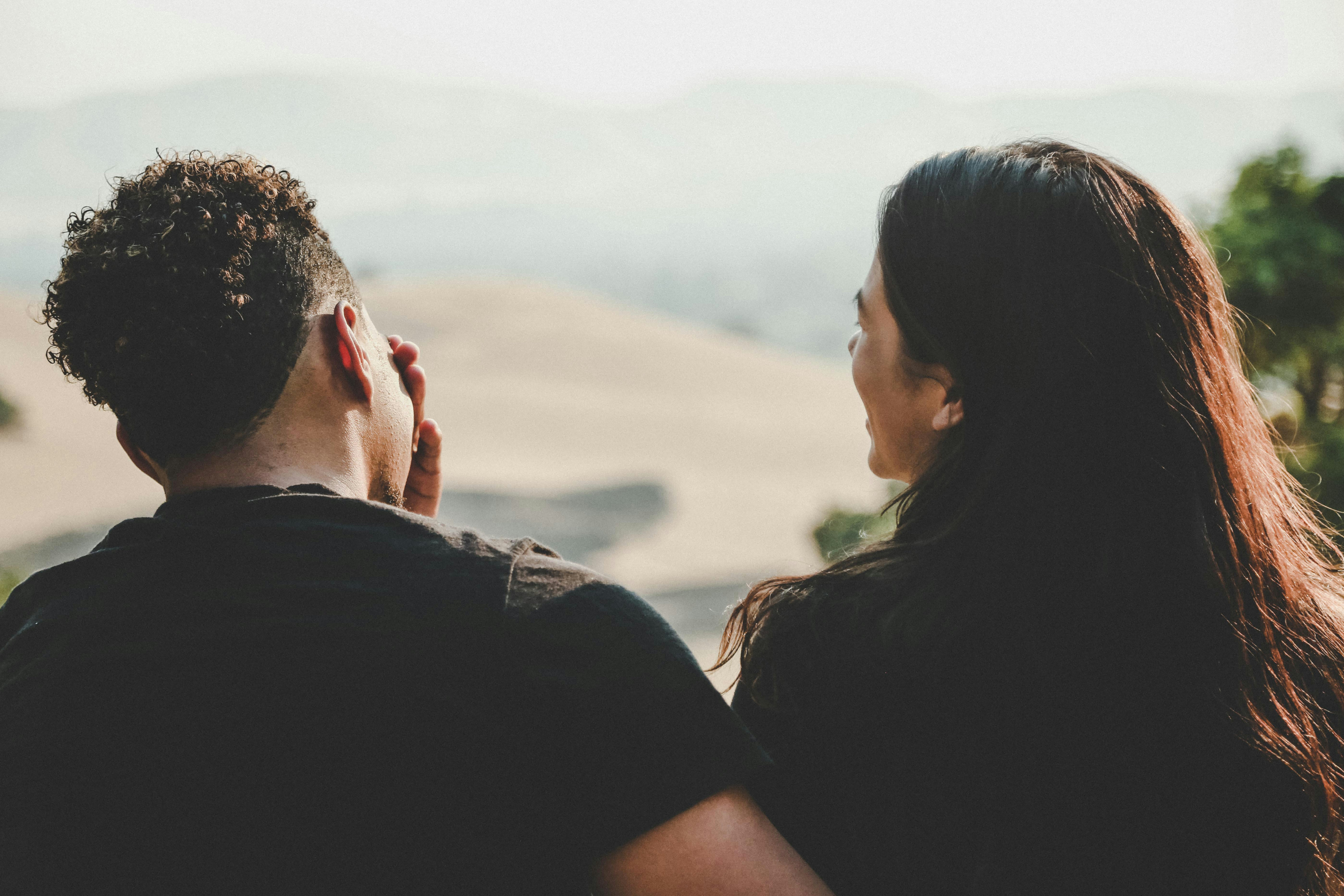 Couple sitting closely outdoors, talking and smiling with a scenic view in the background